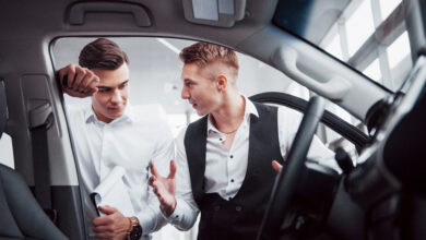 two men stand in the showroom against cars close up of a sales manager in a suit that sells a car to a customer the seller gives the key to the customer