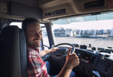 portrait of truck driver sitting in his truck holding thumbs up